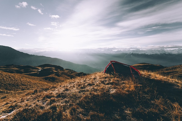 Tent on a grassy mountain ridge with sunlit clouds