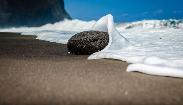 Black sand beach with waves and a rock
