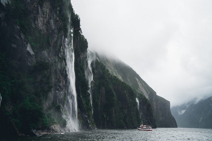 Boat sailing past waterfalls on a cliff face in New Zealand