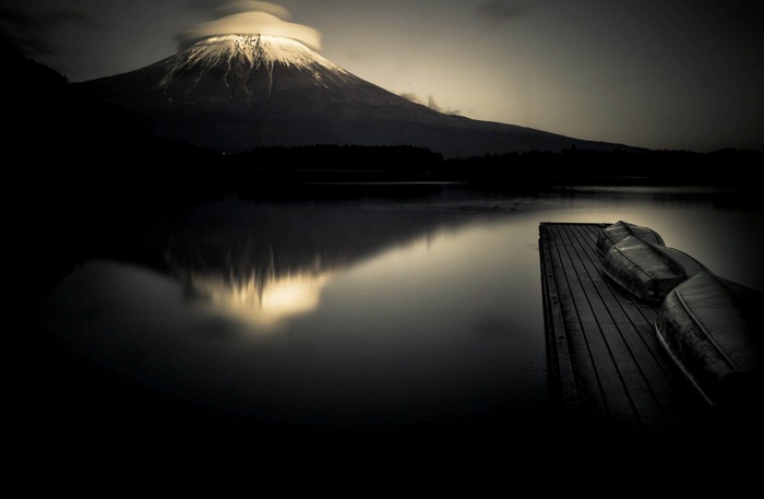 Mount Fuji reflected in a lake with boats on a dock