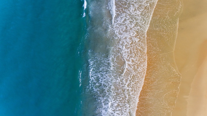 Aerial view of ocean waves crashing on a sandy beach