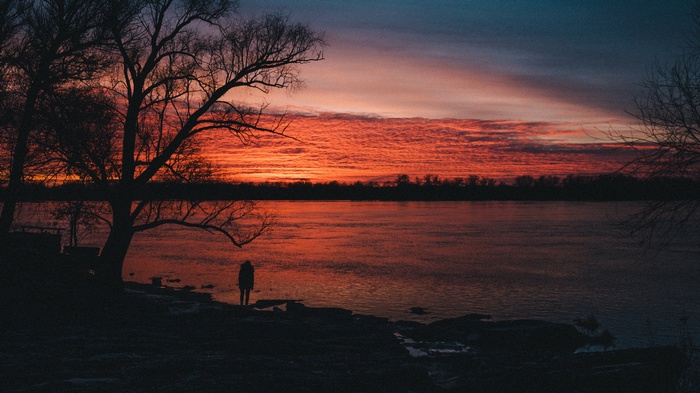 Person standing by a river at sunset