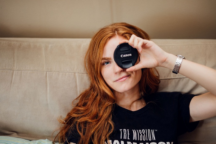 Redhead woman holding Canon lens cap over eye