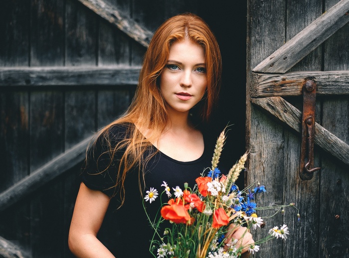 Redhead woman holding flowers in front of a barn door