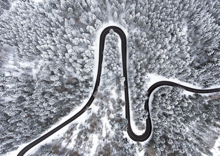 Aerial view of a winding road through a snow-covered forest