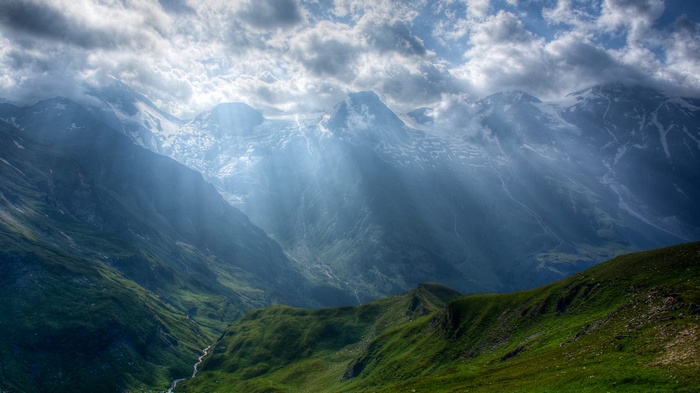 Sun rays over snow-capped mountains and green valley