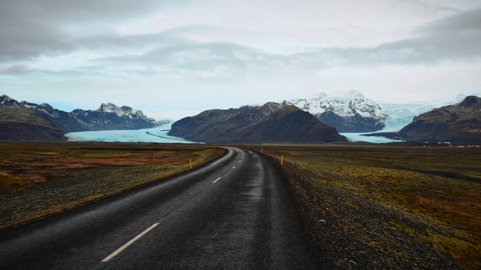 Road leading to a glacier and mountains under clouds