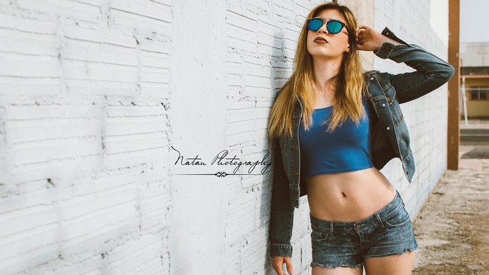 Woman in denim jacket and shorts posing by wall