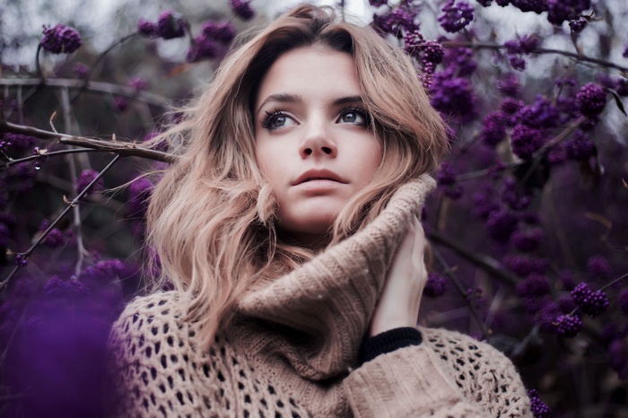 Woman with blonde hair and blue eyes in a sweater near purple flowers