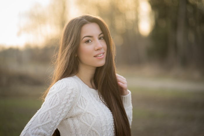 Young woman with long brown hair wearing a white sweater