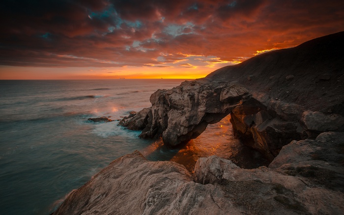 Sunset over rocky coast with natural arch