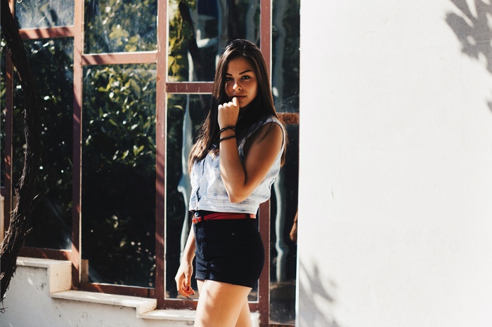 Woman in denim vest and shorts with hand on face