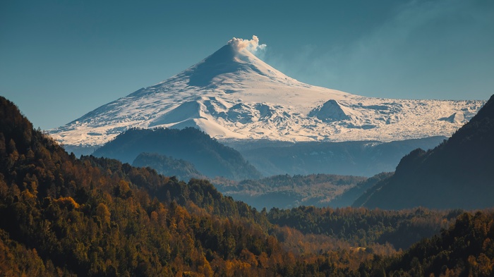 Volcano erupting with smoke over a forest