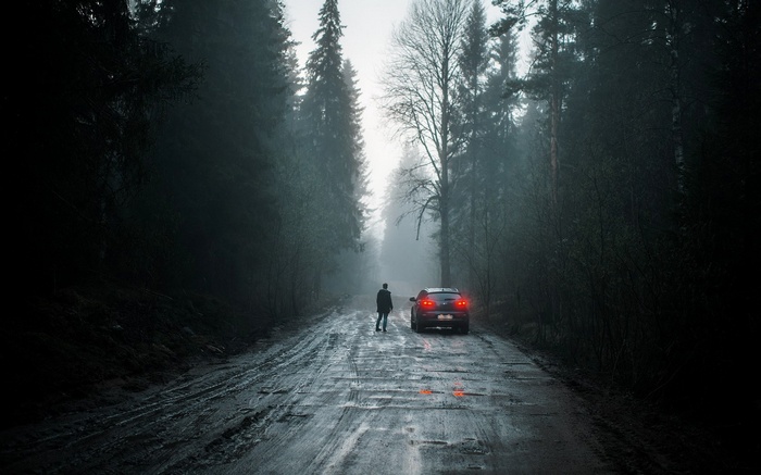 Man standing on a muddy road next to a car in a forest