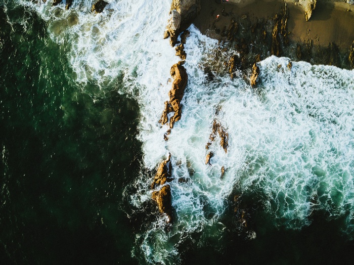 Aerial view of ocean waves crashing on rocky shore