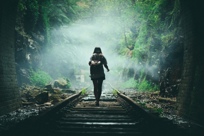 Woman with backpack walking on railway tracks through misty forest