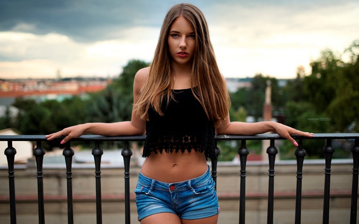 Woman in black crop top and denim shorts on balcony