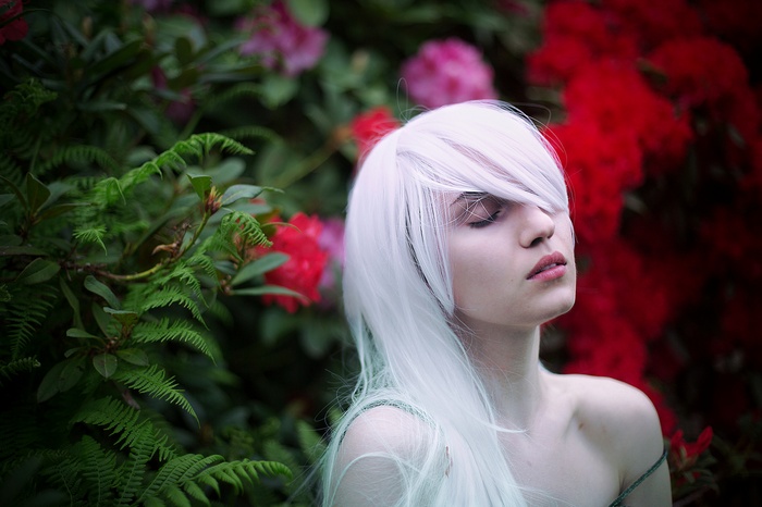 Woman with platinum blonde hair and bare shoulders in front of flowers