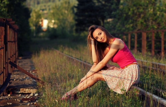 Woman in pink top and skirt sitting on railway tracks