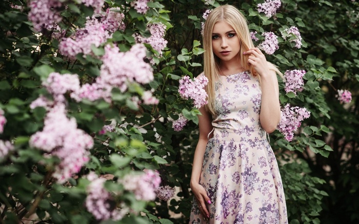 Blonde woman in floral dress near lilac bush