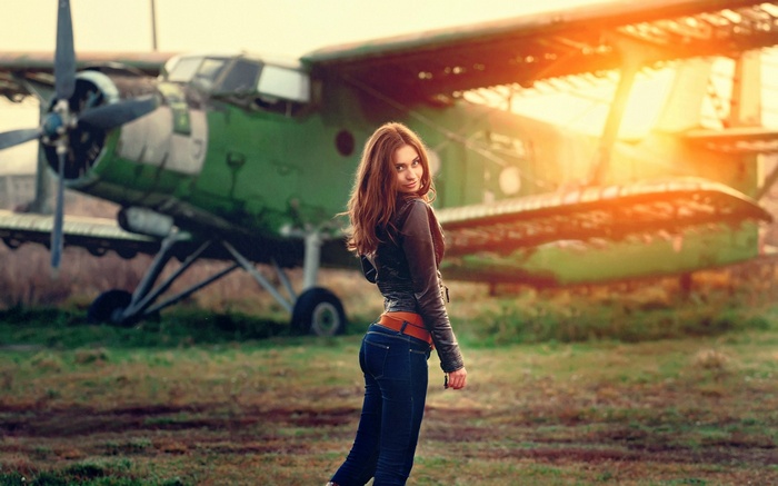 Woman in leather jacket and jeans posing near an airplane