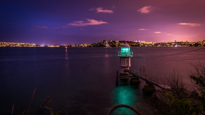 Lighthouse on water at dusk with city lights