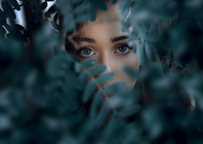 Woman peeking through dark green leaves