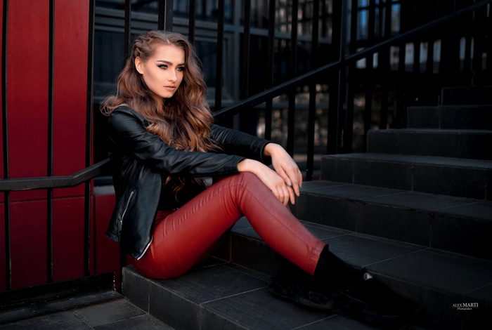 Woman in leather jacket and red pants sitting on stairs