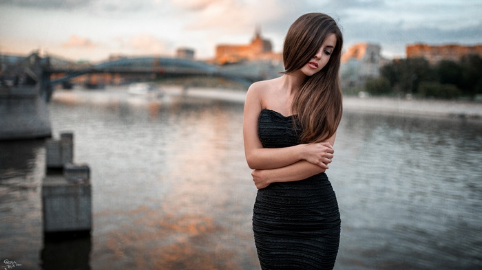Woman in black dress by the river with cityscape