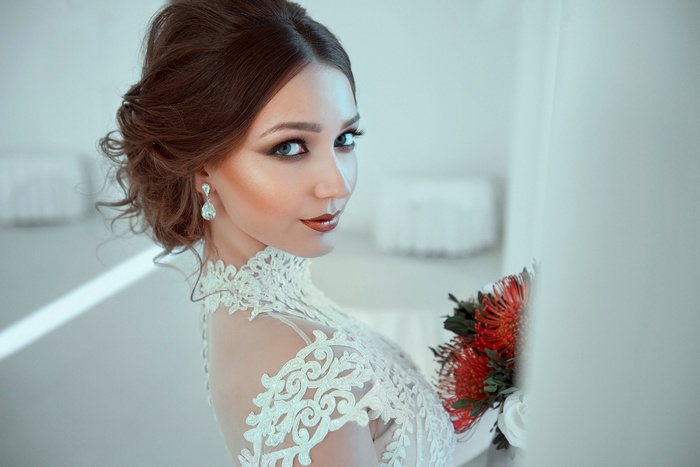 Woman with elaborate hairstyle and wedding dress holding flowers