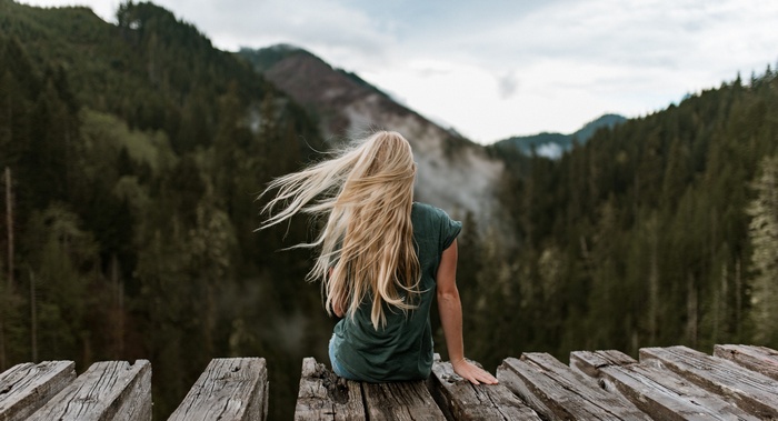 Woman with blonde hair sitting on wooden planks overlooking mountains