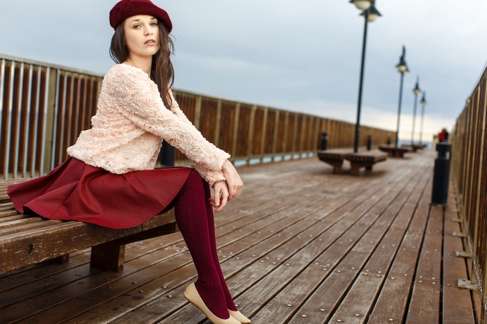 Woman in red skirt and beret sitting on a pier