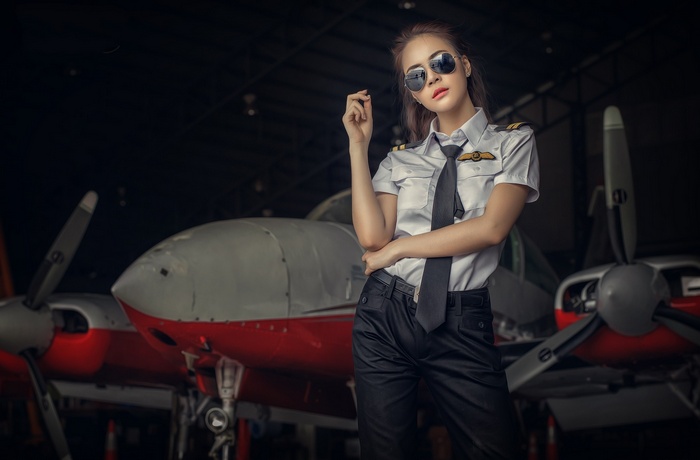 Woman pilot in uniform posing in hangar with airplane