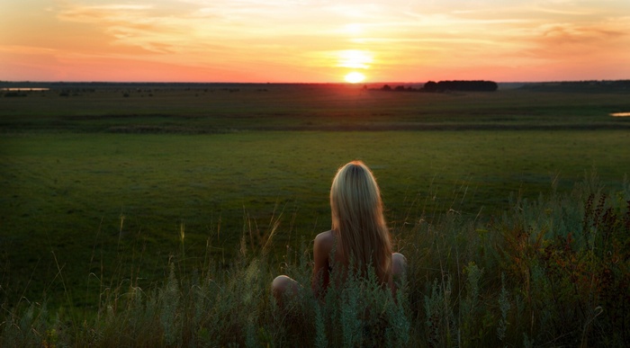 Woman sitting in grass watching sunset