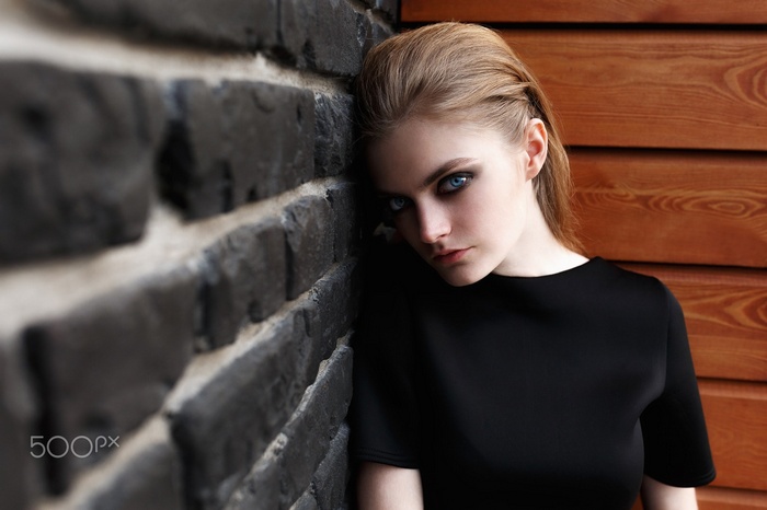 Woman with blue eyes and smoky eyes leaning against a brick wall