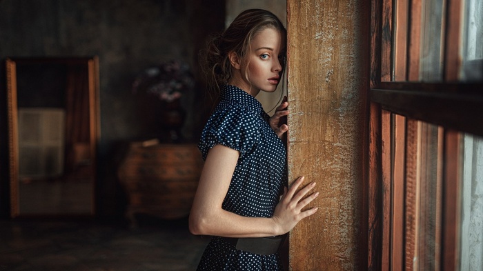 Woman in polka dot dress leaning against wooden pillar
