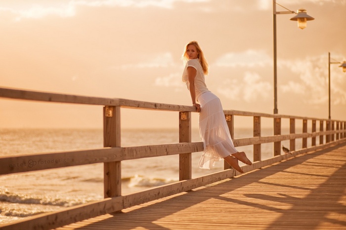 Woman in white dress on a pier at sunset