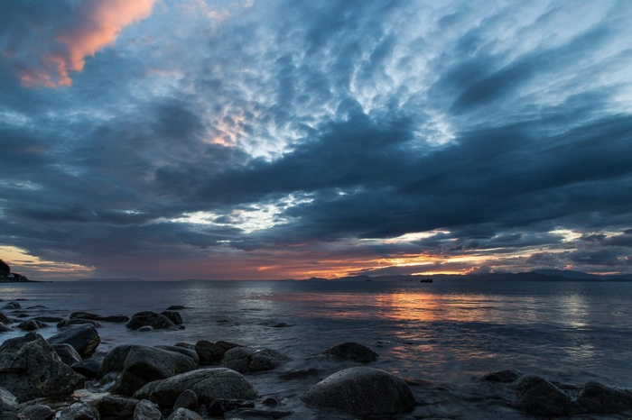Sunset over the ocean with clouds and rocks