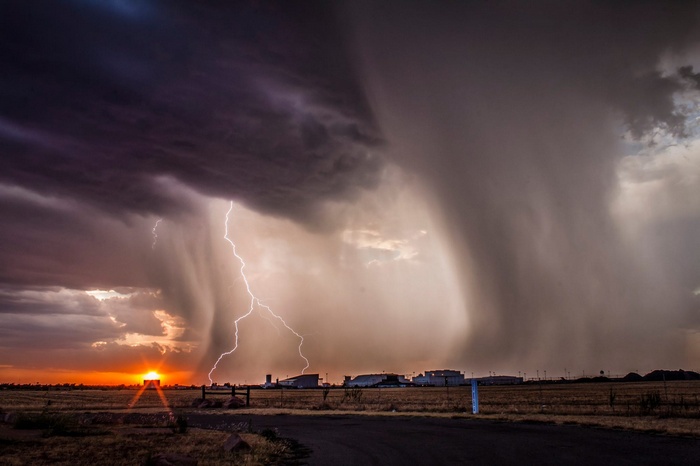 Lightning strikes during a sunset storm over a rural landscape
