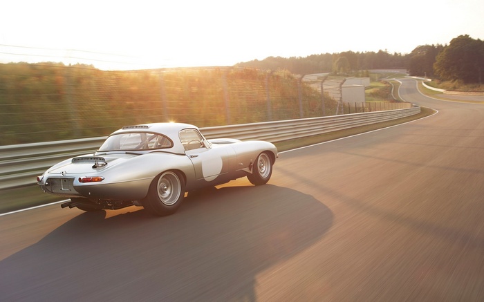 Silver Jaguar E-Type racing on a track at sunset
