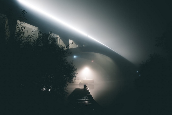 Person sitting on a dock under a bridge at night