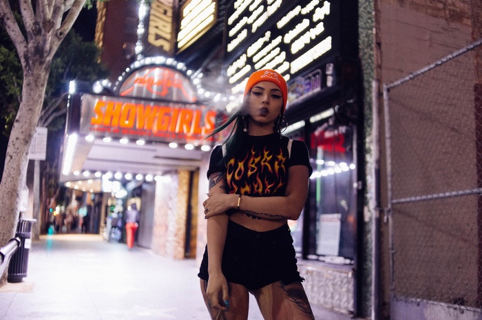 Woman in flame T-shirt and beanie smoking outside Showgirls
