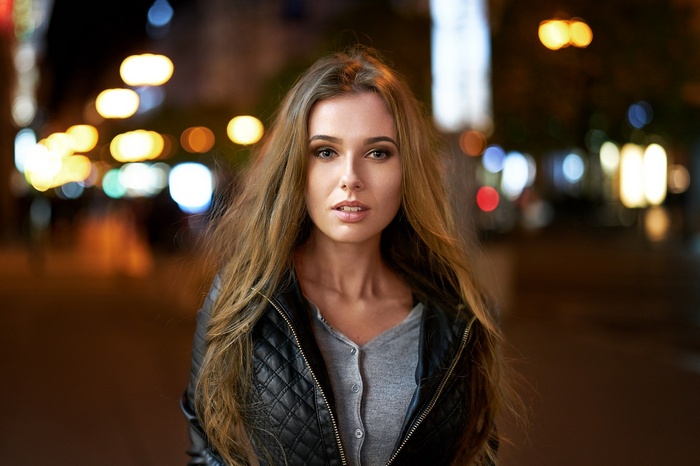 Woman with long blonde hair wearing a leather jacket at night