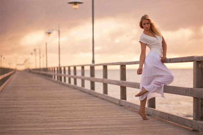 Woman in white dress on a pier at sunset