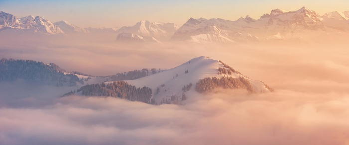 Snow-covered mountains above clouds at sunrise