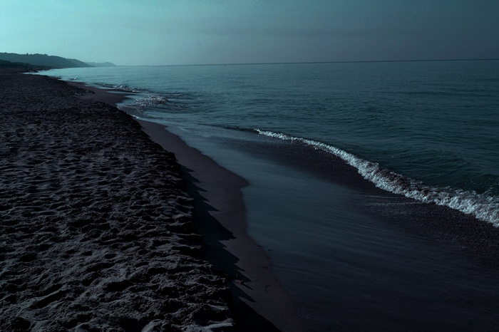 Dark beach with waves and sea under overcast sky