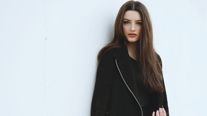 Woman in black coat with red lipstick against white wall