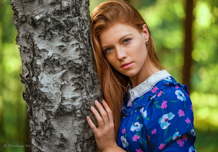 Redhead woman leaning against a birch tree