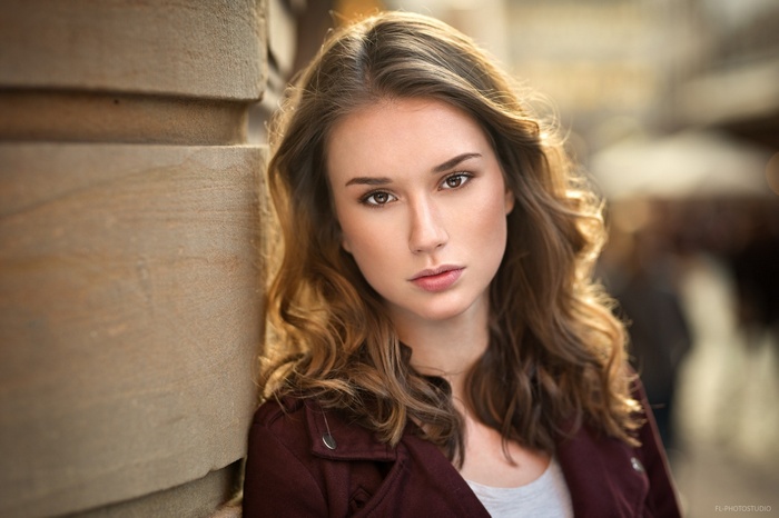 Woman with brown hair leaning against a stone pillar