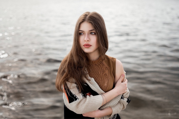 Woman with long brown hair and red lipstick by the water